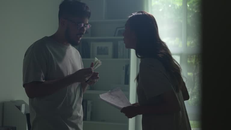 Asian couple arguing about money at home, husband and wife shouting in a hard quarrel by their many debts at home, financial family problems concept.
